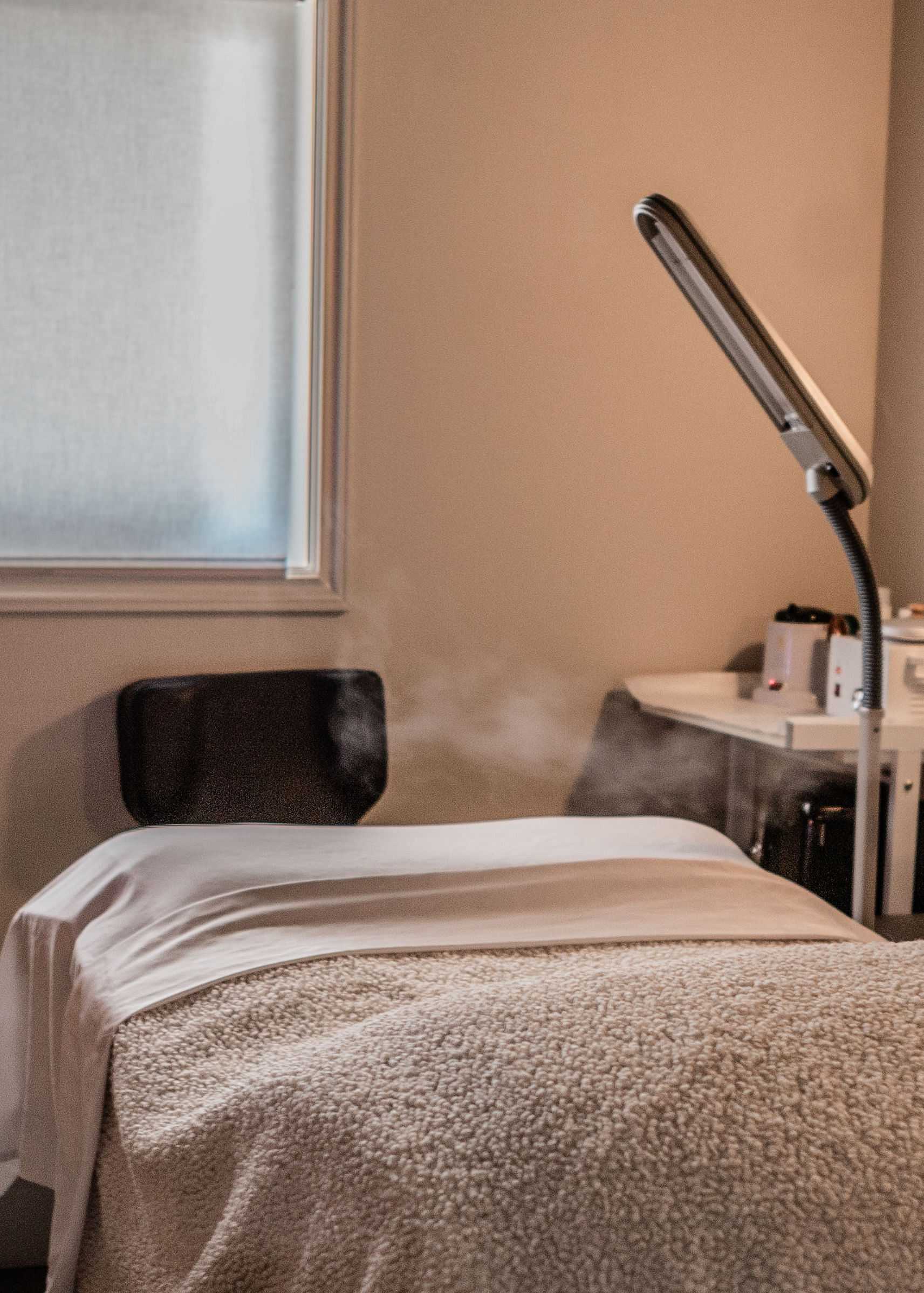 Massage room with a cozy bed, lamp, and steaming aromatherapy diffuser.