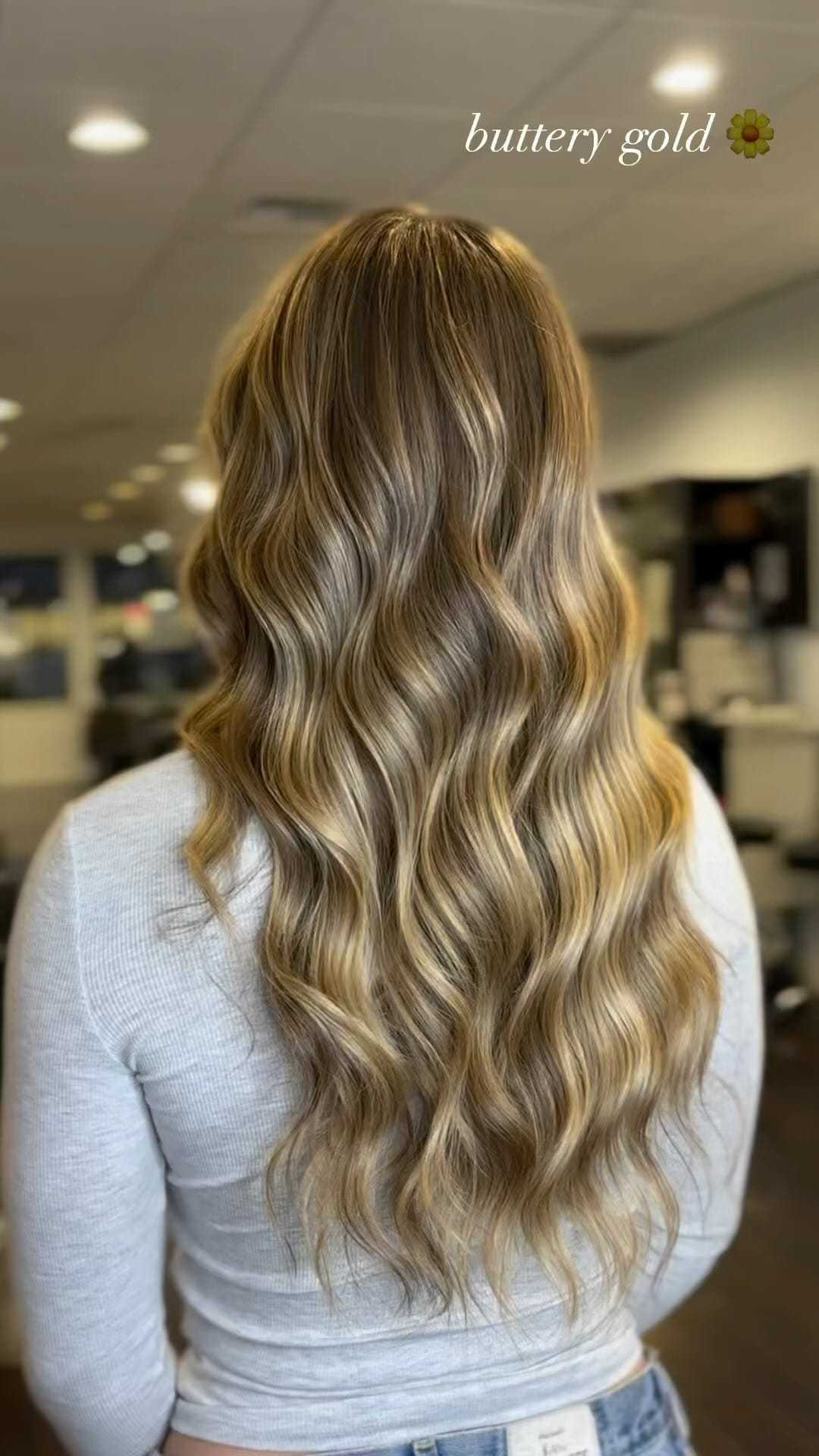 Woman with long, wavy, buttery gold hair, wearing a light gray top in a salon setting.