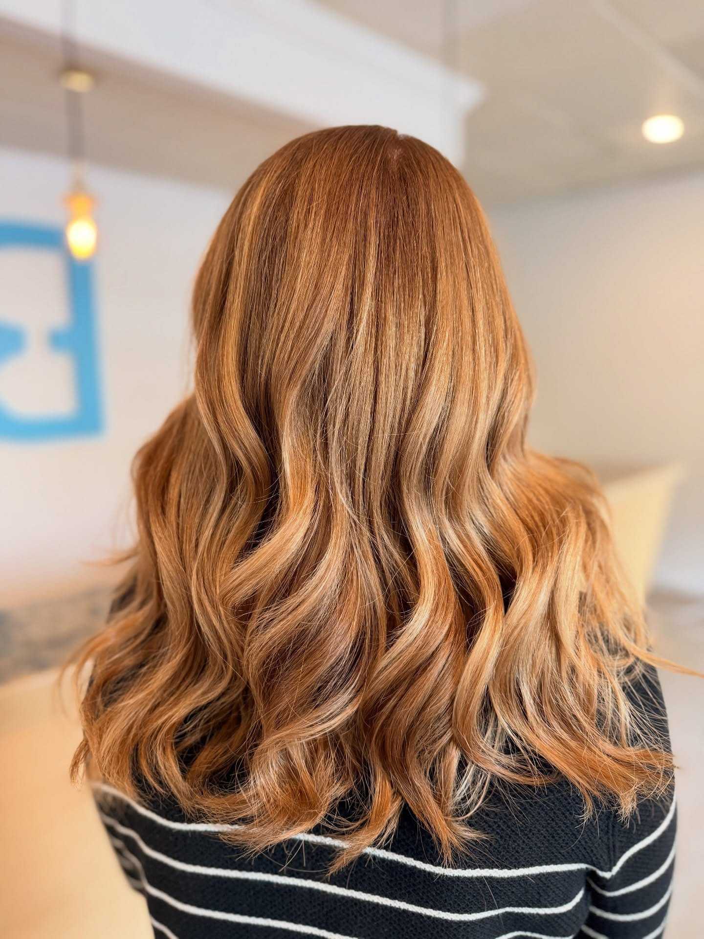 Wavy hairstyle with caramel highlights, viewed from the back.