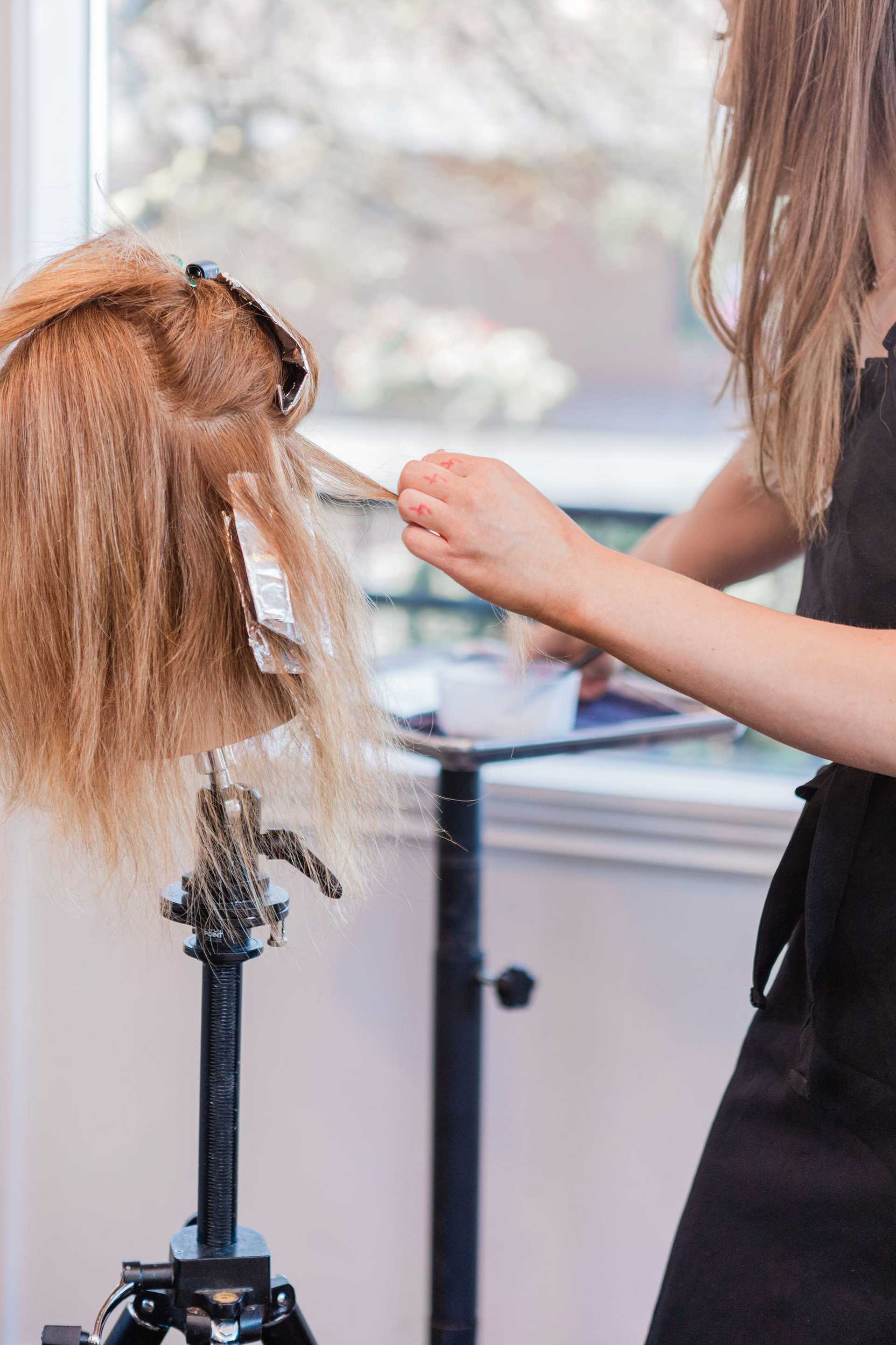 Hairdresser applying highlights to a wig on a mannequin head.