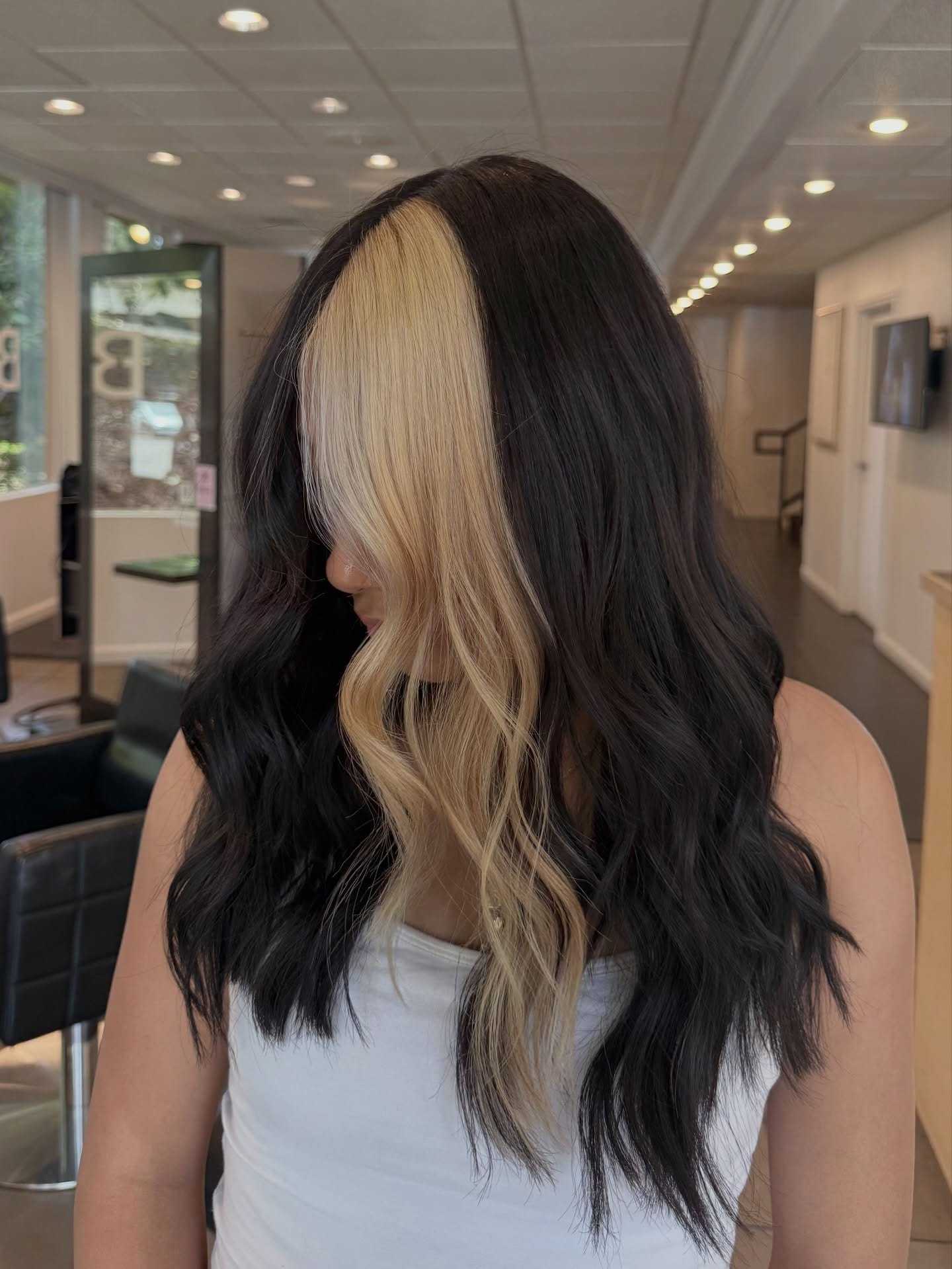 Two-toned hairstyle with one side black and the other side blonde, worn by a woman indoors.