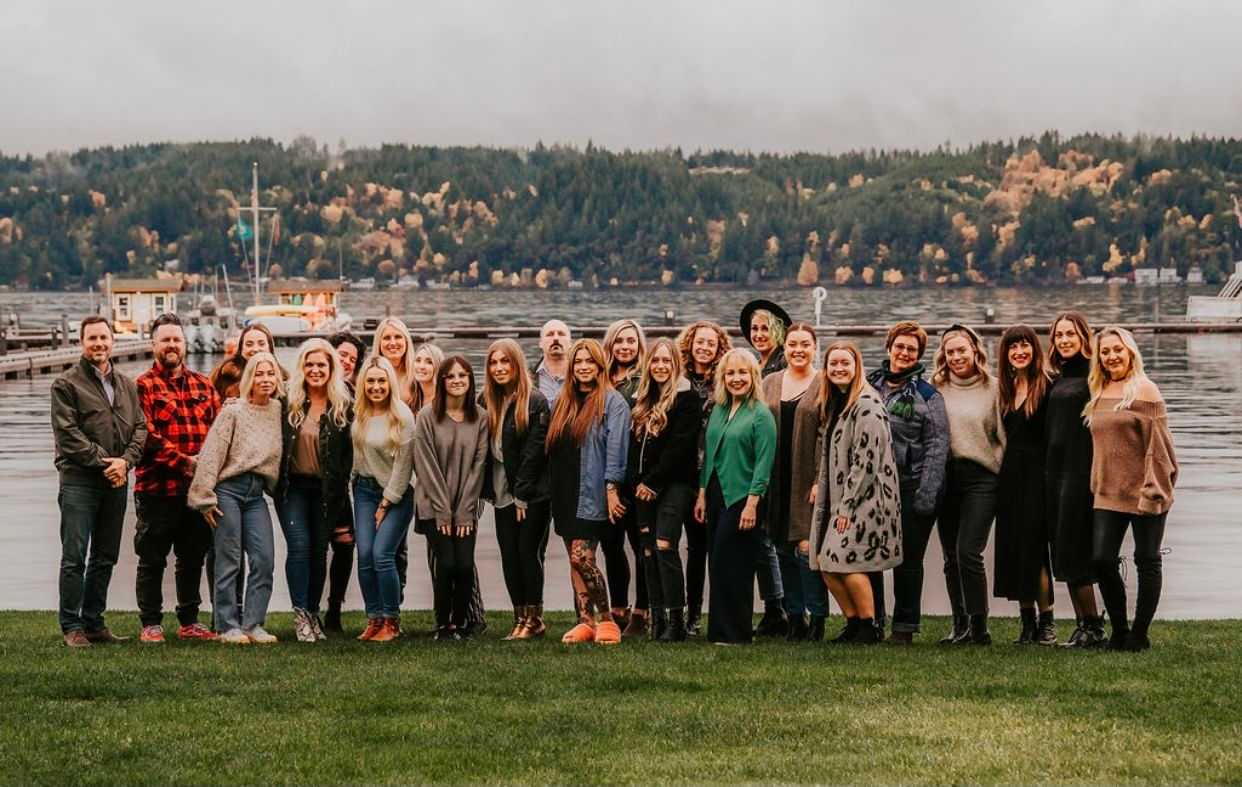 Group of people posing by a lakeside with forested hills in the background.