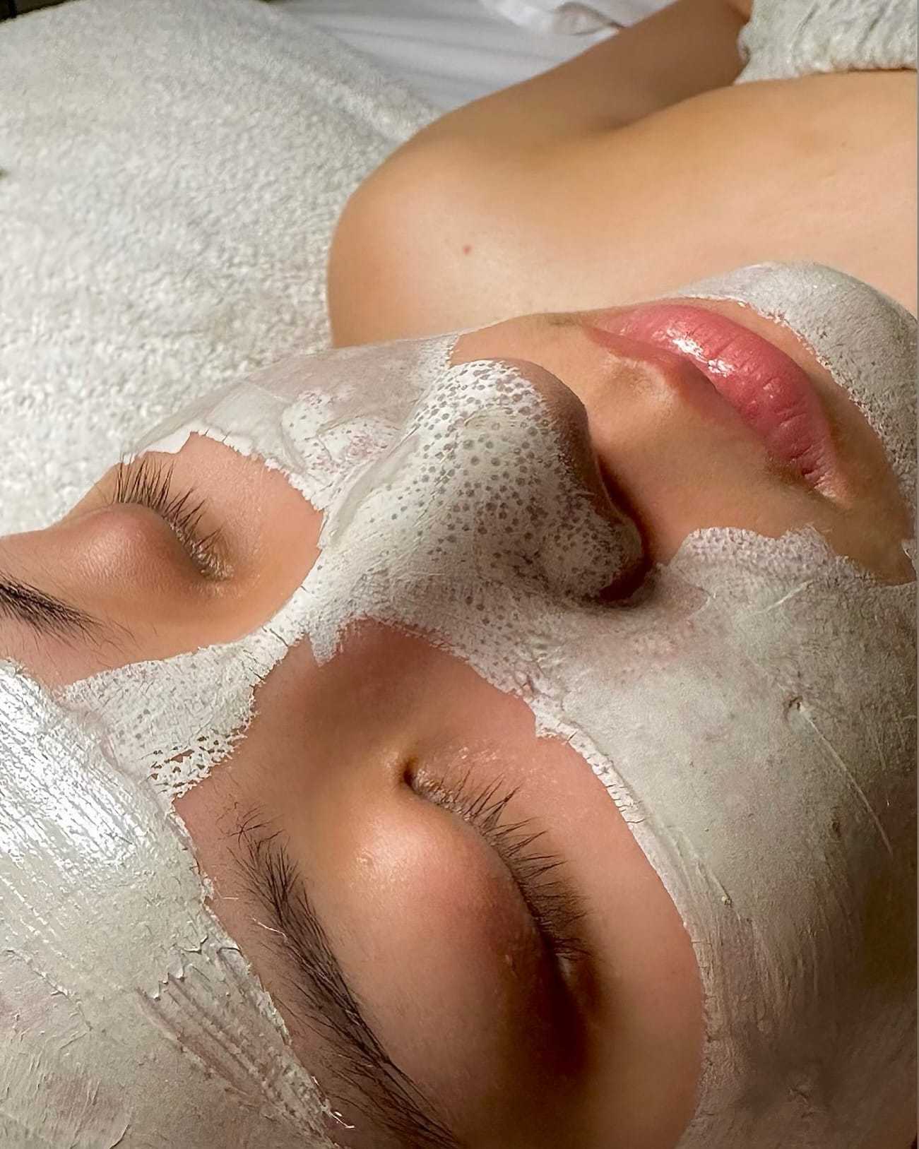 Facial treatment with clay mask on a relaxing woman lying down.