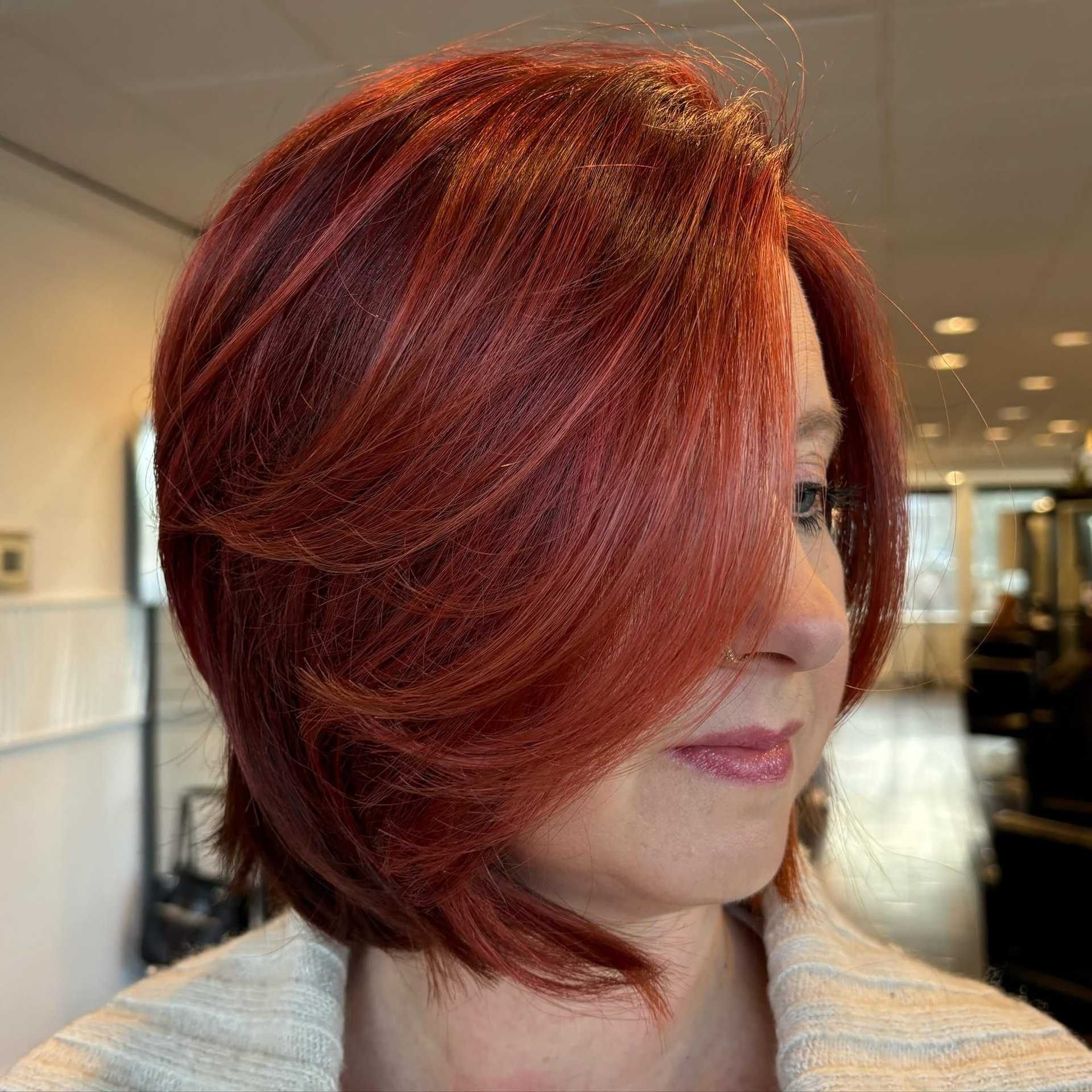Close-up of a person with a stylish red bob haircut in a bright, modern salon.