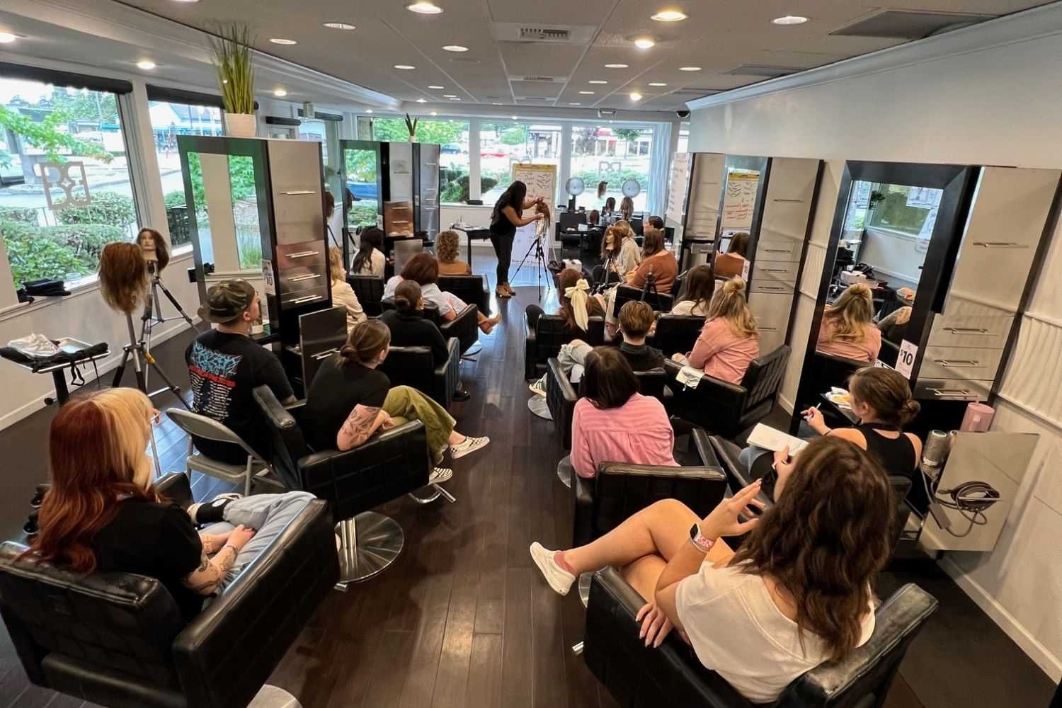 Hairdressing class in a salon with attendees watching an instructor demonstrating techniques.