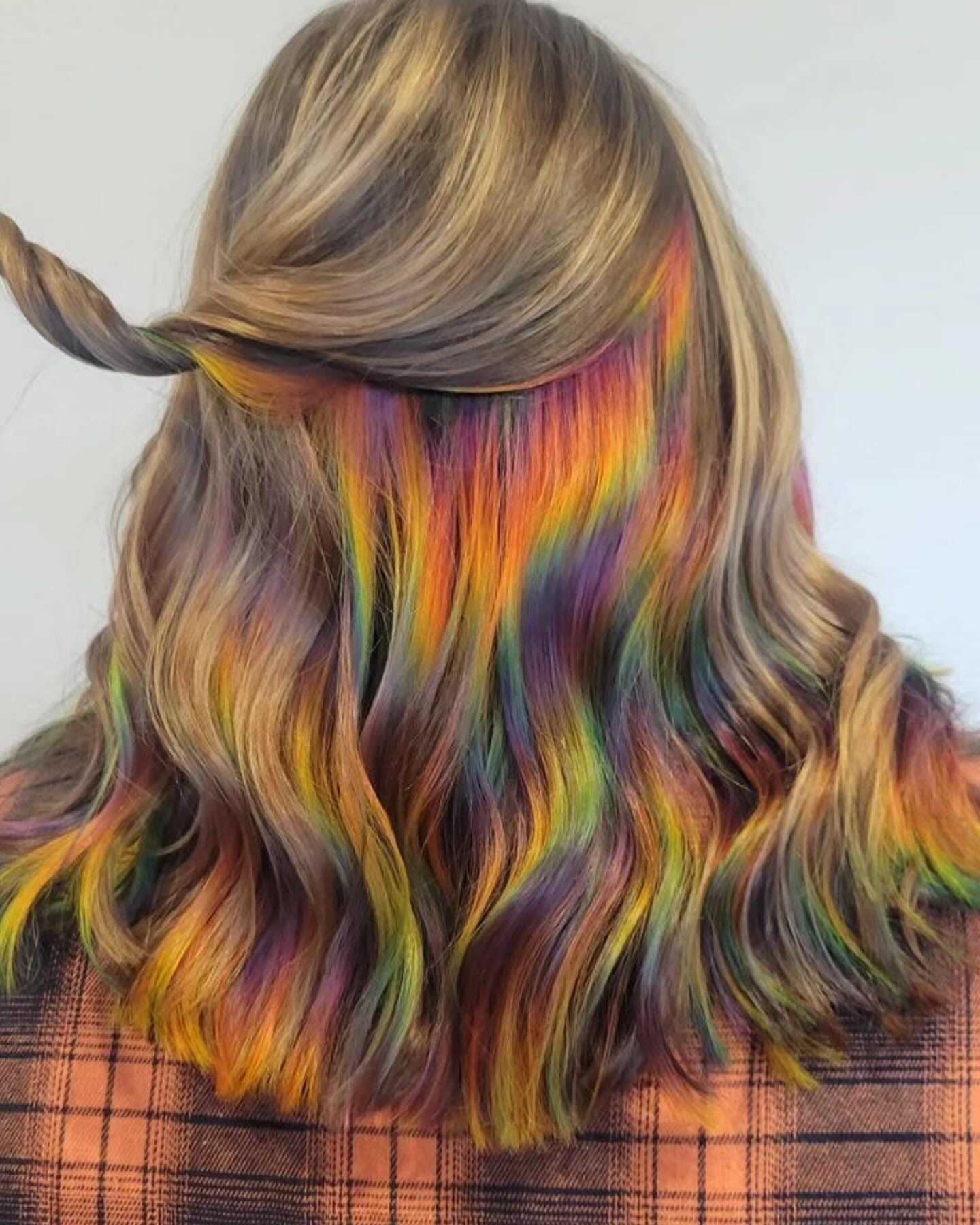 Back view of wavy hair dyed in vibrant rainbow colors, tied partially up, with plaid clothing.